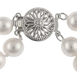 A close-up of a two-strand white pearl bracelet with a decorative silver starburst clasp